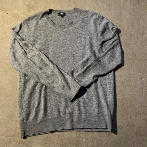 Grå tröja från Uniqlo - Säljer en stilren grå tröja från Uniqlo. Den är långärmad med ribbade muddar och rund hals. Perfekt för en minimalistisk look.