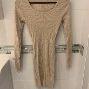 Beige ribbad klänning - Snygg beige ribbad klänning med lång ärm och knappar framtill. Perfekt för en stilren och bekväm look.
