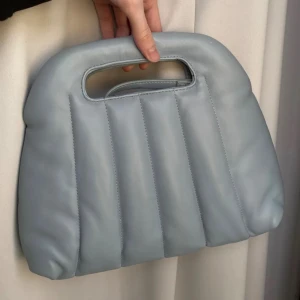 Ljusblå quiltad handväska - Snygg ljusblå handväska med quiltad design och inbyggt handtag. Perfekt för en stilren look och enkel att bära med sig. Väskan har en modern och minimalistisk stil.