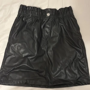 Svart kjol från H&M - Snygg svart kjol i skinnimitation från H&M med elastisk midja och knappdetalj. Perfekt för en trendig look.