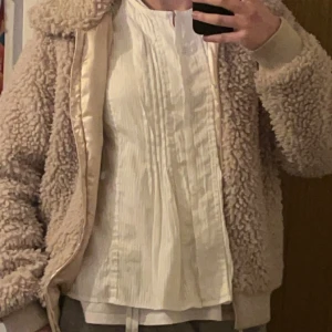 teddyjacka  - Mysig beige teddyjacka med ribbade muddar.  Jackan har fickor på sidorna och även en ficka inne vid bröstet. Storlek 170 men den passar även s/xs.