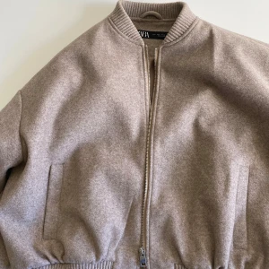 Beige bomberjacka från Zara - Säljer en snygg beige bomberjacka från Zara i storlek S. Jackan har en dragkedja framtill och ribbade muddar vid ärmslut och nederkant. Perfekt för höst och vår! 🧥