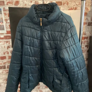 Mörkblå pufferjacka från Antea - Säljer en snygg mörkblå pufferjacka från Antea. Jackan har en quiltad design med dragkedja framtill och är perfekt för kyliga dagar. Den är både stilren och bekväm, idealisk för höst och vinter.