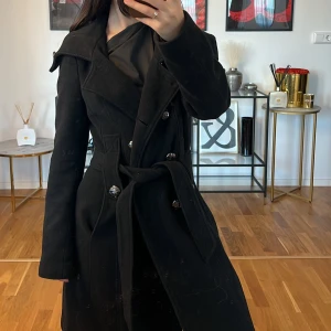 Svart kappa med bälte Calvin Klein  - Säljer en elegant svart kappa från Calvin Klein .Den har en klassisk design med dubbelknäppning och ett bälte i midjan för en snygg passform. Perfekt för höst och vinter, och den är långärmad för extra värme. Kappan är i bra skick💓