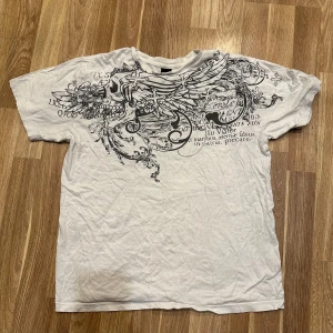 Vit t-shirt med tryck - En vit t-shirt med ett coolt svart tryck på framsidan. T-shirten har korta ärmar. Perfekt för en avslappnad stil! Storlek M