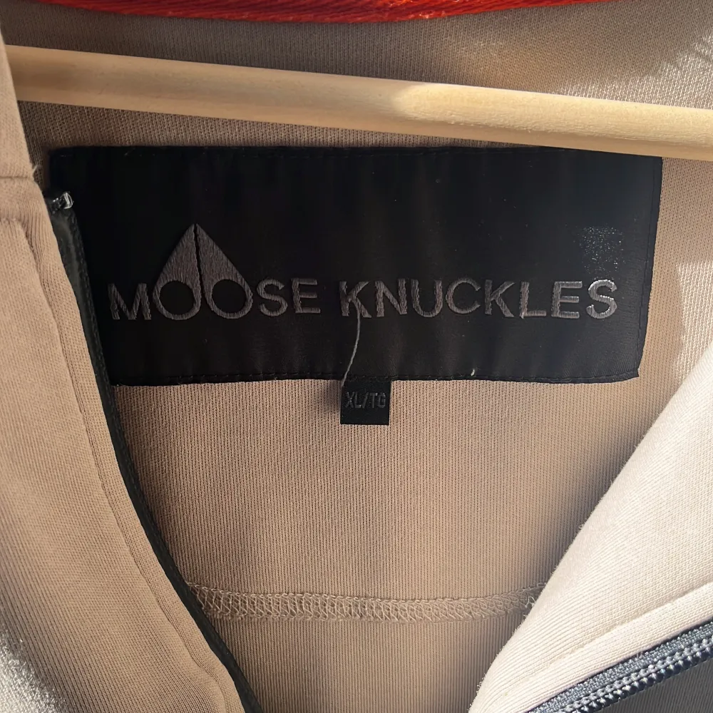 Säljer en snygg beige hoodie från Moose Knuckles. Den har en dragkedja framtill och en cool logga på bröstet. På baksidan av huvan finns det en text som ger den en unik touch. Knappt använd. Nypris 2600kr. Tröjor & Koftor.