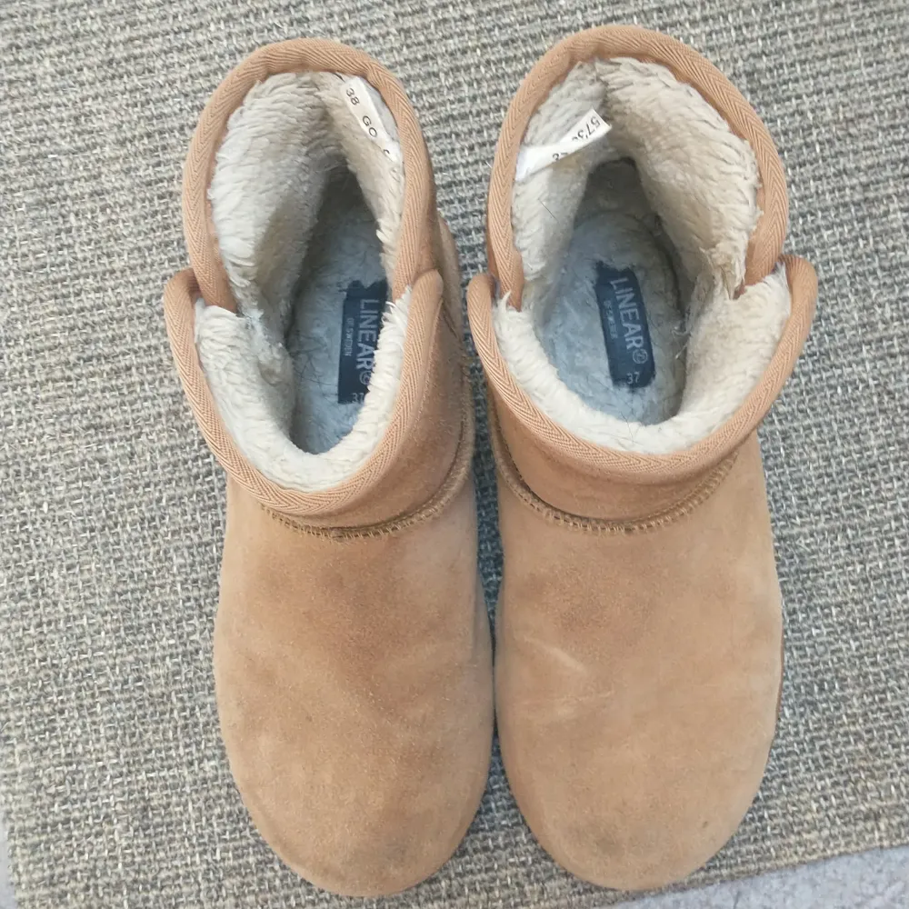 Säljer ett par mysiga bruna skor i mocka med mjukt foder inuti. De har en enkel design med en liten flik bak för att lättare ta på sig dem. Skorna är välanvända med några märken på ytan, men går helt bra att använda hör av er om frågor!Nypris: 500kr. Kengät.