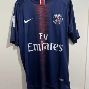 Paris Saint-Germain fotbollströja Neymar Jr - Säljer en snygg Paris Saint-Germain fotbollströja med Neymar Jr och nummer 10 på ryggen. Tröjan är mörkblå med röda och vita detaljer, och har Fly Emirates som sponsor på framsidan. Den är kortärmad och perfekt för alla PSG-fans!