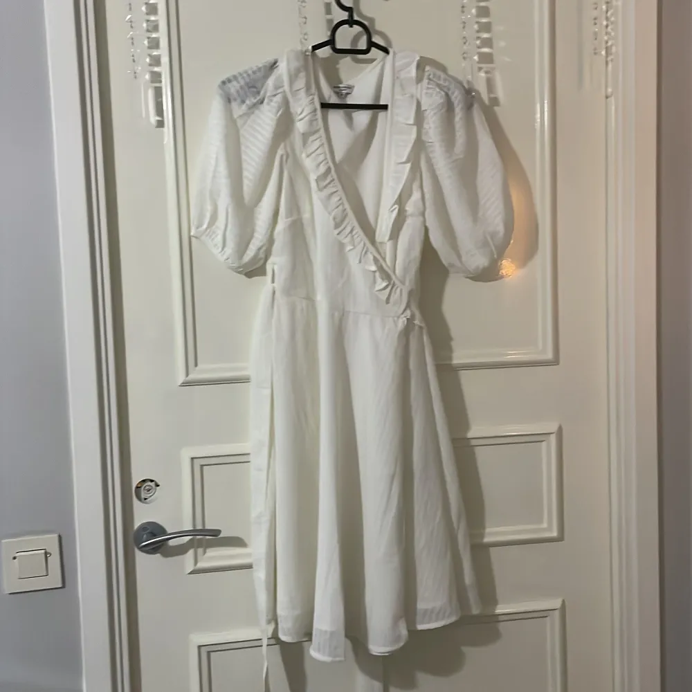 Säljer en elegant vit omlottklänning med volangdetaljer och puffiga trekvartsärmar. Klänningen har en knytning i midjan och en v-ringad design. Klänningen är använd en gång men är som ny och är från bubbleroom☺️. Mekot.