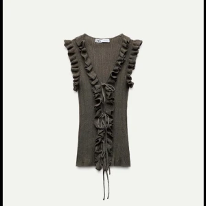 Olivgrön ribbad topp från Zara - Säljer en olivgrön ribbad väst från Zara med volangdetaljer och knyt framtill. Västen har en v-ringad design och är perfekt för lager-på-lager-stil. Passar bra till både jeans och kjol.