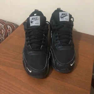 Svarta Nike Air Max sneakers - Snygga svarta Nike Air Max sneakers med klassisk design och vit swoosh-logga på sidan. Skorna har snörning och en synlig luftdämpning i sulan för extra komfort. Perfekta för en stilren look.