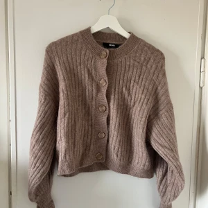 Beige/brun ribbad kofta från Bik Bok - Mysig beige kofta från Bik Bok med ribbad struktur och stora knappar framtill. Bra kvalitet. Sparsamt använd. 