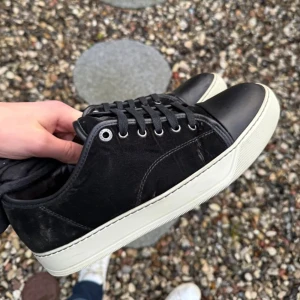 Svarta sneakers från Lanvin - Snygga svarta sneakers från Lanvin med vit sula och snörning. Skorna har en stilren design med en kombination av mocka och skinnmaterial. Perfekta för en casual look.