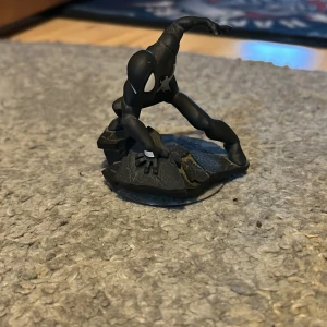 Svart Spiderman Disney infinite  - Säljer en cool svart Spiderman från Disney infinite. Figuren står i en actionfylld pose på en stenliknande bas. Perfekt för samlare eller som dekoration. Märkt med Marvel 2.0 under basen. Kom gärna med prisförslag!
