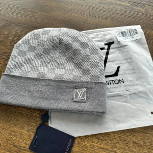 Grå rutig mössa  - Snygg grå mössa med ett klassiskt rutigt mönster. Mössan har en uppvikt kant och en diskret logotyp framtill. Perfekt för att hålla sig varm med stil. Pris kan diskuteras 