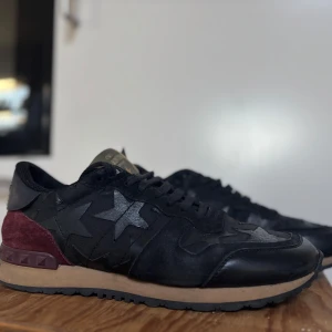 Valentino rockrunners  - Snygga svarta sneakers från Valentino med stjärndetaljer och nitar på hälen. Skorna har en kombination av skinn och mocka med en cool stjärndesign. Köpta från sellpy 