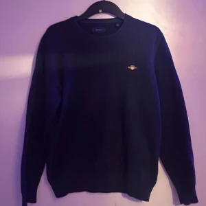 Marinblå tröja från GANT - Snygg marinblå tröja från GANT med ett diskret märke på bröstet. Använd några få gånger och väldigt bra skick. Tveka inte på frågor!