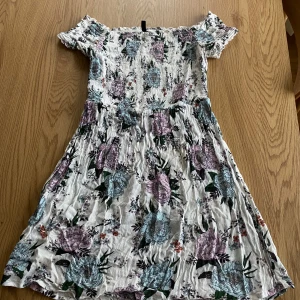 Blommig klänning från H&M Divided - Säljer en söt blommig klänning från H&M Divided. Klänningen har korta ärmar och ett vackert blommönster i lila och blå toner på en vit bakgrund. Perfekt för sommarens alla tillfällen! 🌸