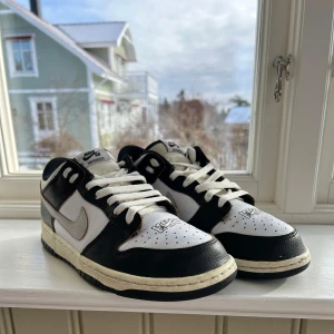 Nike SB Dunk Low HUF - Snygga Nike SB Dunk Low HUF i svart och vitt med broderade detaljer. Skorna har snörning och en unik design med texten 'KEITH FOREVER' på hälen. Perfekta för sneakerheads som vill ha något speciellt. Original pris 5000:-. Jag köpte dem i San Francisco . Dom här skorna gjordes för att fira 20år  vilket också står på insidan 