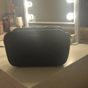 Svart axelväska från L'éternité - Snygg svart axelväska från L'éternité med silverkedja och dragkedja. Perfekt för att bära dina nödvändigheter med stil. Enkel och elegant design som passar till många tillfällen.