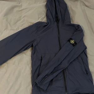 Mörkblå jacka från Stone Island Junior - Säljer en snygg mörkblå jacka från Stone Island Junior. Jackan har en huva och dragkedja framtill. Perfekt för en stilren look. Säljer den för den är förliten, den har inga defekter och är en 10/10 i skick! Dm för mer information! 😀