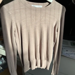 Beige tröja från Zara - Säljer en stilren beige tröja från Zara med långa ärmar och dekorativa knappar vid ärmsluten. Perfekt för en elegant och avslappnad look. Tröjan har en rund halsringning och är tillverkad i ett mjukt material. Tröjan har en fläck på magen som jag tror går bort i tvätten men har inte testat. Skriv vid frågor! 💞