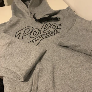 Grå hoodie från Ralph Lauren - Säljer en stilren grå hoodie från Ralph Lauren med stor logga på framsidan. Tröjan har långa ärmar och en praktisk känguruficka. Mycket fint skick på tröjan 😌 Ny pris runt 1500 mitt pris 699, kan gå att pruta ner lite🫡 tröjan passar s-m
