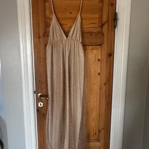 Champagnefärgad långklänning med glittrande  - Elegant champagnefärgad långklänning med tunna axelband och v-ringning. Perfekt för en festlig kväll eller bal.