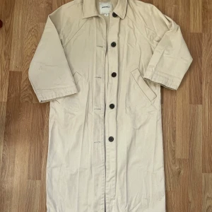Beige trenchcoat - Stilren denimkappa i beige bomull. Storlek xxs men oversize så funkar bra på vanlig xs.  Lite färgad på insidan av kragen och någon fläck nertill, har dock inte testat tvätta så det mesta går nog bort! Inget som jag tycker stör när man bär kappan dock. 