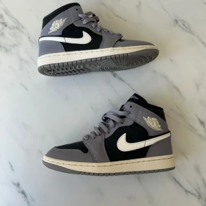 Nike Air Jordans i grått och svart - Snygga Nike Air Jordans i en stilren kombination av grått och svart. Skorna har en klassisk design med snörning och den ikoniska Nike-loggan i vitt på sidan.
