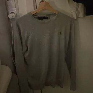 Grå tröja från Polo Ralph Lauren - Säljer en stilren grå tröja från Polo Ralph Lauren med rund halsringning. Tröjan har en liten broderad logotyp på bröstet och långa ärmar. Perfekt för en avslappnad och klassisk look xs passar också s