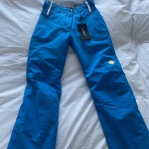 Blå täckbyxor med dragkedja från J.Lindeberg - Snygga blå täckbyxor perfekta för vintern. Nya med prislapp från J.Lindeberg. Nypris 2100kr