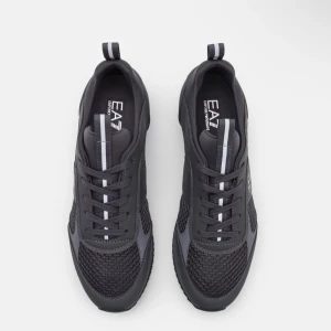 Grå sneakers från EA7 - Snygga grå sneakers från EA7 med en stilren design. Skorna har snörning och är tillverkade i syntetmaterial med meshdetaljer för extra andningsförmåga. Perfekta för en sportig look. Använda 2-5 gånger