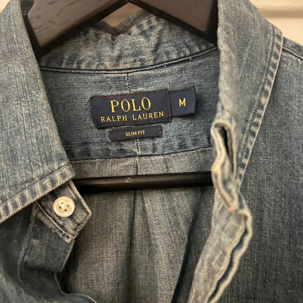 Säljer en snygg jeansskjorta från Polo Ralph Lauren i storlek M. Skjortan har en klassisk krage och knappar hela vägen ner. Den är i en stilren blå färg och har en broderad logga på bröstet. Perfekt för både vardag och fest!. Skjortor.