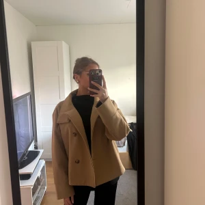 Kort kappa i beige/brun - Säljer min Gina tricot kappa med hög knäppbar krage i storlek S som jag fick i present. Säljer pågrund av att den tyvärr inte kommer till användning. Ändas använt fåtal gånger så den är fortfarande i fint skick💗
