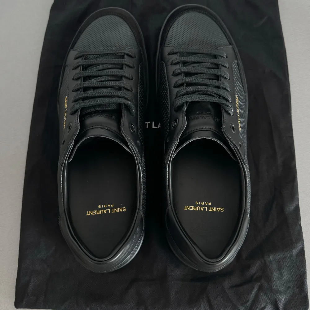 Säljer ett par stilrena svarta sneakers från Saint Laurent. De är i nyskick och tillverkade i Italien. Skorna har en klassisk design med snörning och är gjorda i skinn. Perfekta för både vardag och fest!  Köptes på farfetch för 6700 kr.. Skor.