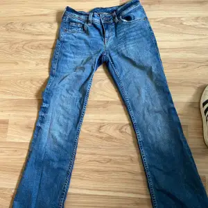 Lågmidjade blå jeans med knappar på bakfickorna.  Lite smått slitna längst ner på ena benet.  Köpte för 250kr