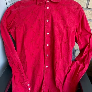 Röd skjorta från Poggianti - Säljer en snygg röd skjorta från Poggianti med ett coolt cirkelmönster. Skjortan har långa ärmar och knappar fram. Perfekt för både vardag och fest! Det finns en liten defekt vid knäppningen, men det är inget som stör helhetsintrycket. Passar perfekt till höst och vår.