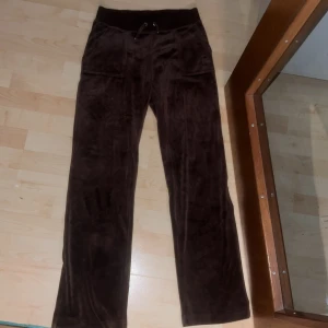 Bruna mjukisbyxor från Juicy Couture - Säljer ett par supermysiga bruna mjukisbyxor från Juicy Couture. De har en loose passform och är perfekta för höst och vinter. Byxorna har en snörning i midjan för bästa passform och är gjorda i ett mjukt material som känns skönt mot huden.