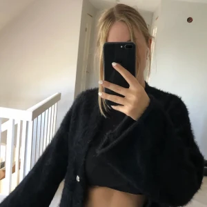 Svart fluffig kofta - Säljer en supermysig svart kofta med fluffigt material. Den har långa ärmar och knäpps med en knapp framtill. Perfekt för att hålla sig varm och stilren under höst och vinter. Passar till både vardag och fest!