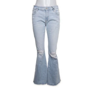 Ljusblå bootcut jeans med slitningar - Säljer ett par snygga ljusblå bootcut jeans med coola slitningar på knäna. De är lågmidjadd och har en klassisk femficksdesign. Perfekta för en avslappnad men ändå trendig look!