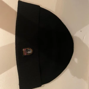 Svart mössa från Parajumpers (RIB HAT)  - Snygg svart mössa från Parajumpers med broderad logga framtill. Perfekt för kyliga dagar med sin ribbade design som ger en skön passform. En stilren mössa för både vardag och utomhusaktiviteter. Från Kidzbrandstore och kostar 899kr ny.