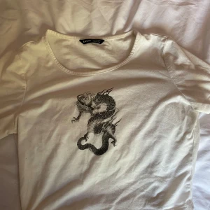 Vit t-shirt med draktryck från Shein - Snygg vit t-shirt från Shein med ett coolt draktryck i svart på framsidan. Perfekt för en avslappnad stil med en touch av edge. Gjord i mjukt material för bekväm passform. Använd ca 1-2 gånger 