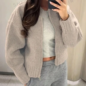 Beige stickad kofta - Snygg beige stickad kofta med dragkedja framtill. Koftan har en oversized passform och långa ärmar, perfekt för kyliga dagar. Den mjuka stickade texturen ger en mysig känsla.