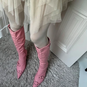 Rosa stövletter med klack - Snygga rosa stövletter med spetsig tå och hög klack. Skorna har dekorativa spännen och dragkedja på insidan för enkel på- och avtagning. Super coola och sköna! Aldrig använda, bara på bild (se bild) lappen på baksidan är kvar. Statement skor! Sitter tajtare mot vaden. Nypris 520kr, asos.