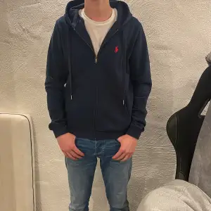 Säljer en snygg mörkblå hoodie från Ralph Lauren med dragkedja och det klassiska röda logotypen på bröstet. Perfekt för en avslappnad stil. 170-180cm skulle jag rekommendera. Självklart äkta, Aldrig använd. Skriv om ni har några funderingar