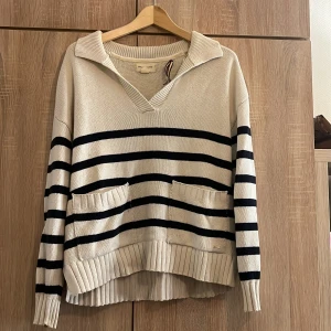 Randig tröja från Holly & Whyte by Lindex - Säljer en superfin randig tröja från Holly & Whyte by Lindex i storlek M. Den är beige med svarta ränder och har en snygg v-ringning. Perfekt för både höst och vår! Tröjan är i bra skick och har ribbade muddar och två fickor framtill. Markerad storlek M men passar även L