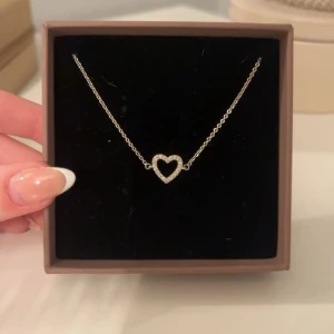 Armband med hjärta i silver - Elegant halsband med ett glittrande hjärta i silver. Perfekt för att ge en subtil men stilfull touch till din outfit. Kedjan är tunn och smidig, vilket gör den bekväm att bära hela dagen.