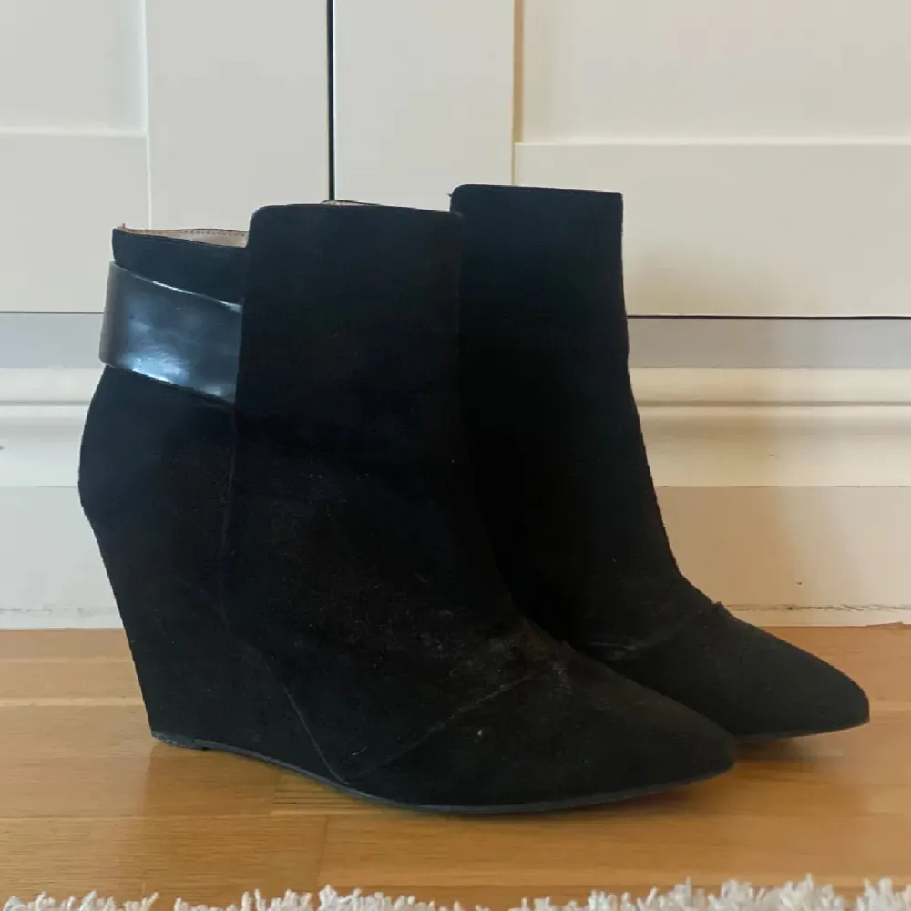 Snygga svarta boots med kilklack och spetsig tå. De har en stilren design med en bred remdetalj upptill. Perfekta för både vardag och fest, och ger en elegant touch till vilken outfit som helst.. Skor.