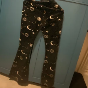 Svarta byxor med stjärnmönster - Säljer ett par svarta byxor med coolt mönster av månar, stjärnor och solmotiv. De är i ett mjukt material och har en bekväm passform. Perfekta för en avslappnad stil eller en mysig hemmakväll. Passar bra till en oversized tröja eller hoodie.